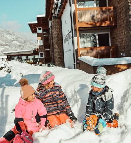Drei Kinder spielen im Schnee vor dem Mia Alpina