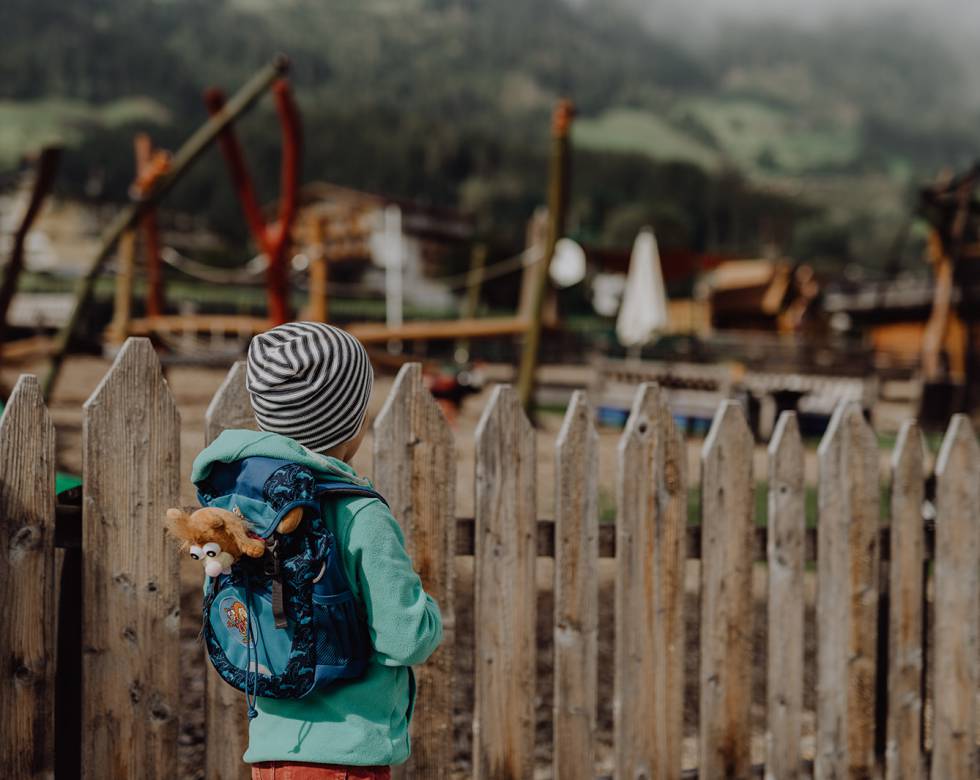 Junge mit Rucksack steht am Spielplatz des Mia Alpina